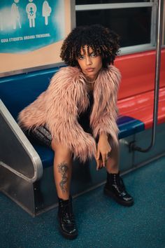 a woman sitting on a subway bench wearing a pink fur coat and black boots with her legs crossed