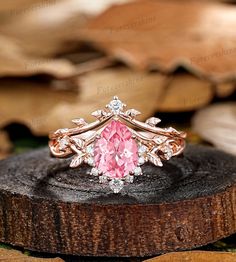 a pink diamond ring sitting on top of a piece of wood with leaves in the background