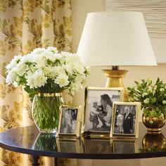 a table topped with two vases filled with white flowers next to pictures and a lamp