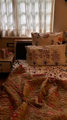 a bed with pillows and blankets on top of it in front of a window filled with curtains