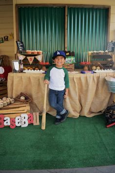 a young boy holding a baseball bat in front of a table with food on it