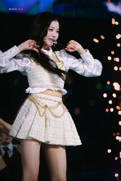 a woman in a short skirt and white shirt is standing on stage with lights behind her