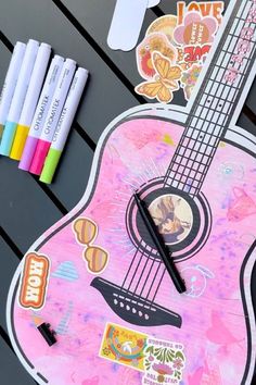 a pink guitar clock sitting on top of a wooden table next to markers and pens