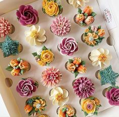 cupcakes decorated with colorful flowers are displayed in a box