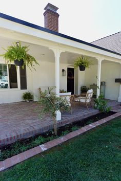 a white house with two chairs and plants on the front porch, next to a brick walkway