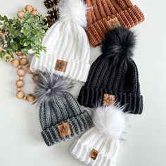 three knit hats with pom - poms on top of each other next to pine cones