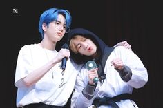 two young men with blue hair are holding microphones