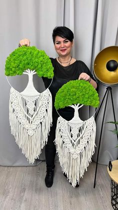 a woman is holding up two trees made out of grass and plants with fringes on them