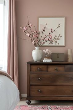 a bedroom with pink walls and a white vase filled with flowers on top of a dresser