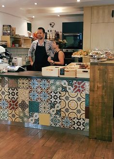 a man standing behind a counter in a kitchen next to a woman and another person