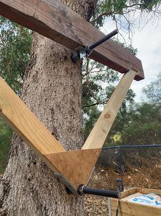 a wooden structure attached to a tree in front of a metal fence and some trees