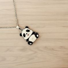 a black and white panda bear pendant on a silver plated chain necklace with a wooden background