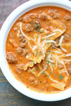 a white bowl filled with soup and meatballs on top of a wooden table next to a spoon