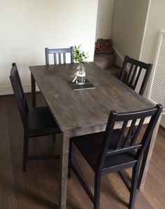 a wooden table with black chairs and a vase on top of it in a living room