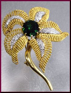 "The captivating flower brooch has a center oval shaped 10.00 ct deep forest green tourmaline. It dates from the 1960's. It is surrounded by 4 gold coiled leaves encrusted with 1.75 ct of round diamonds in the center of each leaf. It all gracefully blooms out of the golden stem. This is enticing appeal all swathed up into a pin. The pin weighs 45 grams. It measures 2 ½ \" long and 2\" wide at its widest point. P 518S SIX MONTH LAY-AWAY AVAILABLE - PLEASE CONTACT ME TO SET UP A PLAN" Luxury Green Brooch For Formal Occasions, Luxury Green Brooch For Anniversary, Luxury Green Brooches For Anniversary, Elegant Green Flower Brooches, Green Fine Jewelry Brooches For Wedding, Fine Jewelry Green Brooches For Anniversary, Green Fine Jewelry Brooch For Anniversary, Fine Jewelry Green Brooch For Anniversary, Luxury Green Brooches For Wedding