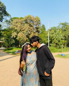 a man and woman standing next to each other on a brick road with trees in the background