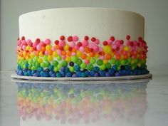 a multi colored cake with white frosting and sprinkles on the top