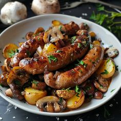 a white plate topped with sausages and potatoes next to mushrooms, parsley and garlic