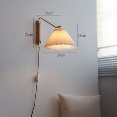 a wall lamp with a white shade on it next to a pillow and window sill