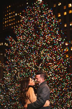 a man and woman standing in front of a christmas tree with lights all around them