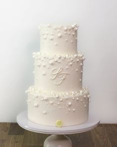 a three tiered white wedding cake with pearls on the side and monogramming