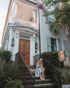 a woman is sitting on the steps in front of a white house with blue shutters