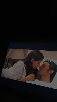 a man and woman laying in bed with the tv screen showing them as if they are kissing