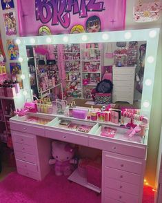 a pink vanity with lights on it and a teddy bear in the mirror next to it