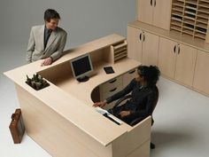 a man and woman sitting at a desk in front of a computer monitor on top of a wooden cabinet