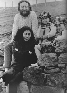 an old black and white photo of people sitting on rocks with one man looking at the camera