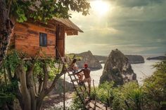 two people climbing up the stairs to a wooden cabin on top of a cliff by the ocean