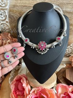 This brass-based textured matte antique silver finish Hasli (necklace style) and dainty earring set has a very gorgeous lotus jadau motif along with dark pink/green or all dark pink  jadau stone work throughout the piece. The color combination with pearl embellishments and ghungooroo embellishments brings the whole piece together really well. The hasli itself is handcarved with beautiful textures through out the piece. Again, this has an antique silver lookalike brass-based metal finish with jadau and kundan stones. The combination of stone color with an antique silver brass-based metal finish makes you look royal with a fusion edge.  The set comes with dainty jadau clear kundan stone with pearl drops. There is a separate picture of earrings, please check it out.  Two color combinations: Handmade Antique Silver Jewelry For Festive Occasion, Festive Handmade Antique Silver Jewelry, Silver Jewelry Sets With Oxidized Finish Pendant, Vintage Silver Jewelry Sets For Festive Occasion, Handmade Silver Temple Jewelry Sets, Traditional Silver Jewelry Sets With Matching Earrings, Handmade Silver Jewelry Sets For Celebration, Silver Temple Jewelry Sets For Gift, Temple Jewelry Sets In Silver, Perfect For Gifts