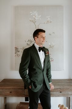 a man in a green suit and bow tie standing next to a table with a teddy bear