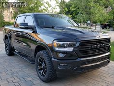 a black dodge ram truck parked in front of a brick driveway with trees and bushes behind it