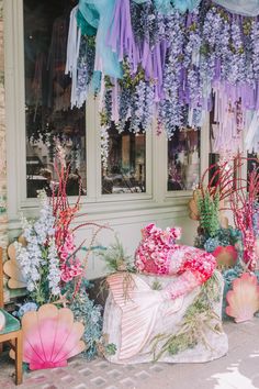 there are many flowers and umbrellas in front of the storefront window that is decorated with ribbons