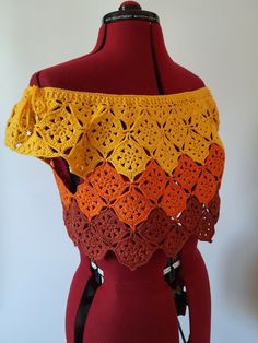 an orange and yellow crochet shawl on top of a mannequin