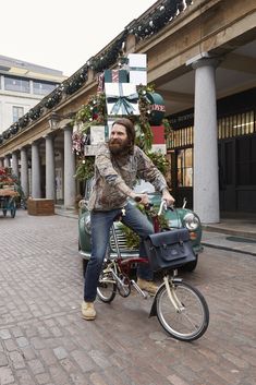 a bearded man on a bike with a christmas tree in the back and decorations around him