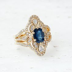 a fancy ring with an oval blue sapphire surrounded by smaller round brilliant cut diamonds on a white background