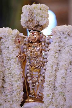 an elaborately decorated statue with white flowers on the sides and gold jewelry hanging from it's neck