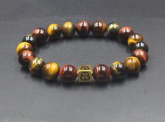 "This designer bracelet features 10mm mixed Tiger's Eye gemstone beads (red, yellow, and blue-green) accented with a 8mm x 8mm 22 karat gold plated sterling silver \"Bali Beads\" logo bead. We use silicon stretch cord for extra strength and resilience. Your bracelet comes in bracelet gift box. Select your bracelet size from the drop down menu. As a general rule, add 1/2 inch to your wrist measurement. Allow 4-6 days delivery time. Check out our other exclusive bracelets for men: https://www.etsy Brown Bracelets With Round Letter Beads, Brown Bracelets With Letter And Round Beads, Beads Logo, Bracelet For Man, Bracelet Man, Man Bracelet, Bracelet Gift Box, Howlite Bracelet, Lapis Lazuli Bracelet