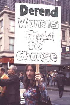 a woman holding a sign that says defend women's right to choose