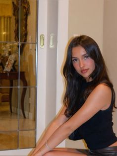 a beautiful young woman sitting on top of a wooden table next to a glass door