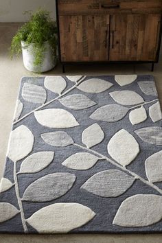 an area rug with leaves on it in front of a cabinet and potted plant