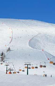 the ski lift is going down the snowy mountain side with many people skiing on it