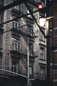 a red traffic light sitting in front of a tall building next to a fire escape