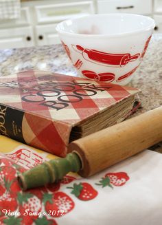 an open book sitting on top of a counter next to a bowl and rolling pin