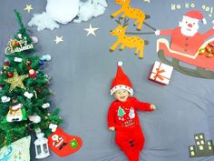 a baby laying on top of a blue blanket next to a christmas tree and decorations