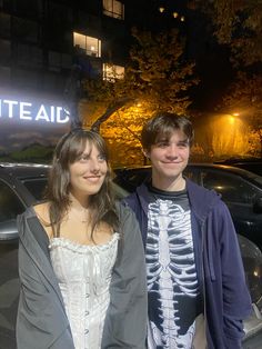 two young people standing next to each other in front of a car at night time