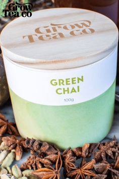 green chai tea in a tin surrounded by various spices and herbs on a table