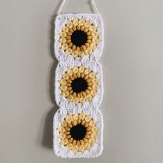 a crocheted wall hanging with three sunflowers in the center and two black centers